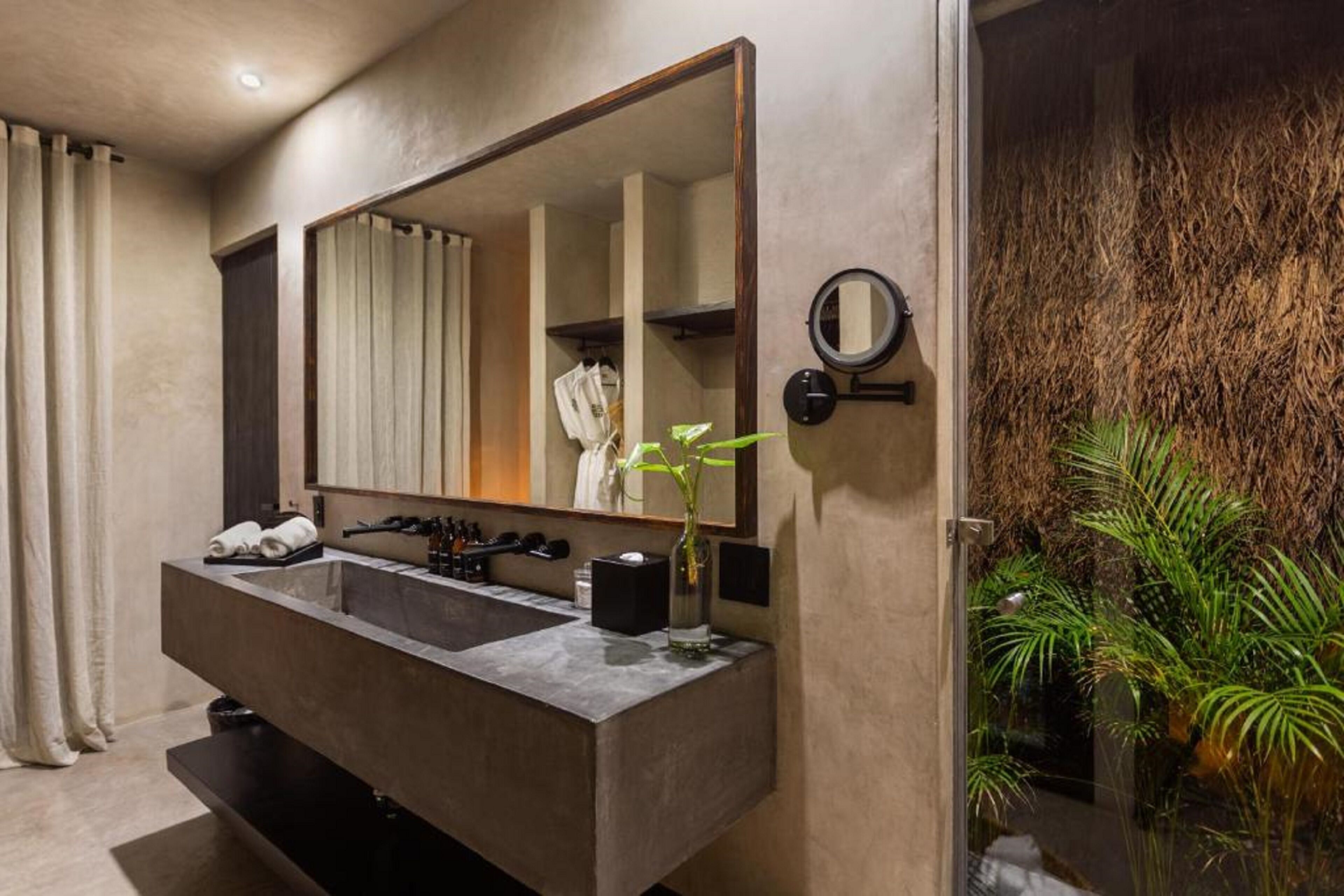 A modern bathroom with a large mirror, dual sinks, and a small plant.
