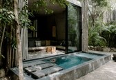 A modern outdoor pool area with a glass enclosure, stone steps, and a seating area with cushions.