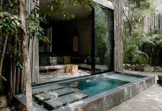 A modern outdoor pool area with a glass enclosure, stone steps, and a seating area with cushions.