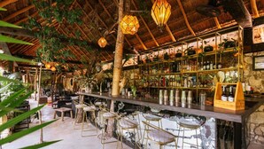 An indoor bar area with a rustic thatched roof, wooden beams, and a variety of bar stools. - Hotel Bardo Adults Only (Tulum)