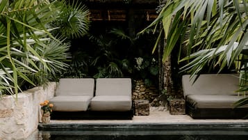 Un área junto a la piscina con dos sofás color beige y un muro de piedra.