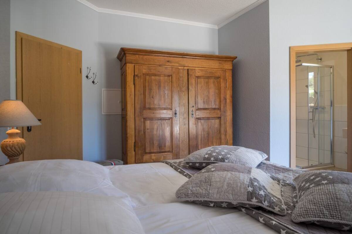 Un dormitorio con cama, un armario de madera, una lámpara y la puerta de un baño.