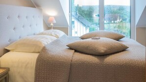 A bedroom with a large bed, a nightstand, a lamp, and a view of the outside through a window. - Hotel Eifellust (Schalkenmehren)