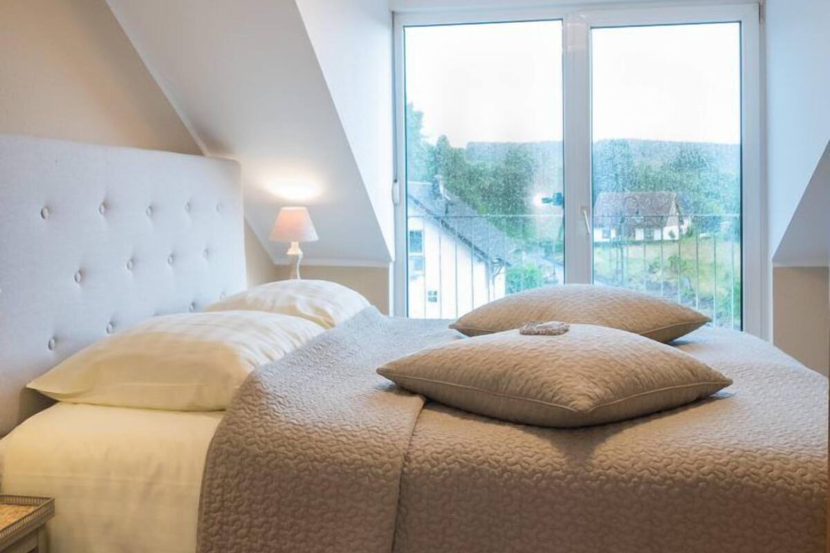 Un dormitorio con una cama grande, una mesita de noche, una lámpara y vistas al exterior a través de una ventana.