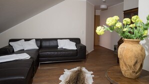 A modern living room with a black leather sofa, a round wooden coffee table, and a large vase with yellow flowers. - Hotel Eifellust (Schalkenmehren)