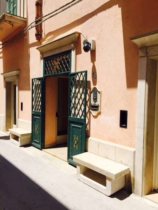 A building with a pink facade, a green gate, and a small bench. - Albergo Ristorante Egadi (Favignana)