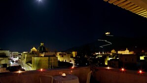 A rooftop terrace with a table set for dining, overlooking a cityscape with illuminated buildings and a clear night sky.