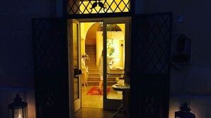 A hotel entrance with a staircase leading to the upper floor, a reception desk, and a small table with a lamp.