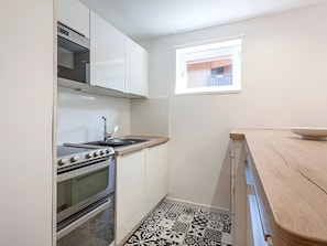 A compact kitchen with white cabinets, a stove, and a window.