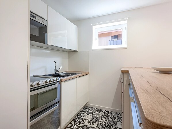 A compact kitchen with white cabinets, a stove, and a window. - Fully Renovated, Near Ski Slopes, Pets Allowed (La Clusaz)