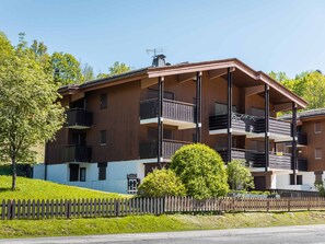 A multi-story building with balconies, a small tree, and a wooden fence.