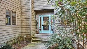 Een houten huis met een blauwe deur, een klein terras en een houten pad naar de deur.