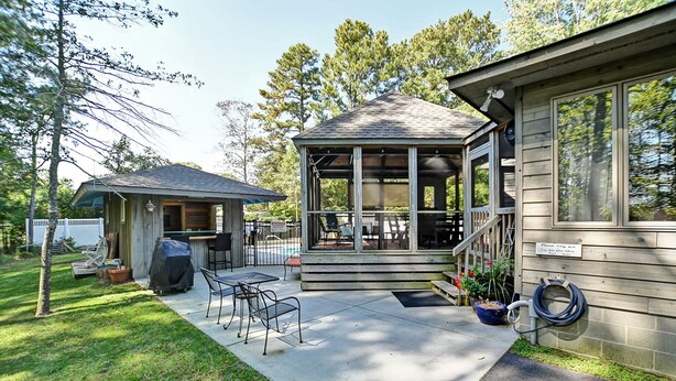 Een klein houten gebouw met een overdekt terras, buitenmeubels en een barbecue.