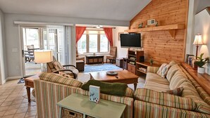 Een gezellige woonkamer met gestreepte banken, een houten tv-meubel en een groot raam met gordijnen.