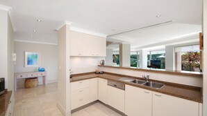 A modern kitchen with white cabinetry, granite countertops, a double sink, and a large window offering a view of the outdoors. - Unit 14  - 3 Bed Garden View (TERRIGAL)
