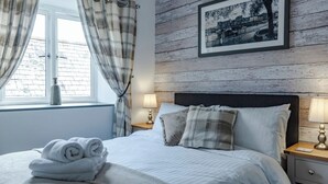 A neatly made bed with rolled towels, a framed picture on the wall, and a window with curtains. - White Lanes by Pureserviced (Plymouth)