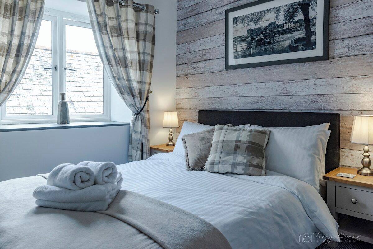 A neatly made bed with rolled towels, a framed picture on the wall, and a window with curtains.