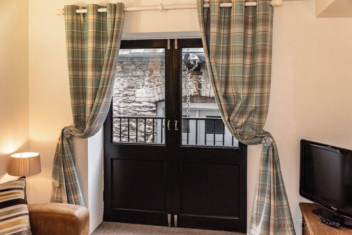 A room with a black door, plaid curtains, a television, and a lamp.
