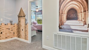 Ein Schlafzimmer mit Wandgemälde zum Thema Burg, einem Bett und einem Fenster mit Jalousien.