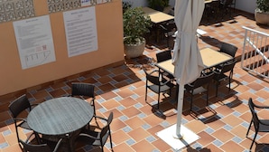 An outdoor patio area with tiled flooring, round tables, and chairs. There are potted plants and a white umbrella. - Hotel Vista Sol (Capdepera)