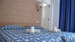A hotel room with a wooden headboard, a patterned bedspread, two rolled towels, a nightstand, and a wall-mounted lamp. - Hotel Vista Sol (Capdepera)