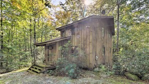 A wooden cabin with a staircase leading up to a deck, surrounded by a forest.