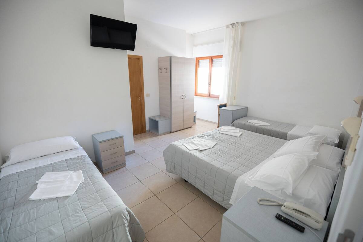 Habitación de hotel con dos camas, un armario, televisor, mesita de noche y ventana con cortinas.