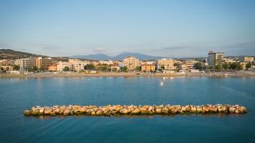 A coastal cityscape with a calm sea, buildings, and a rocky breakwater.