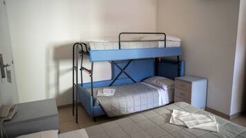 Een stapelbed met een bureau en een klein kastje, een telefoon op een tafel, en een raam met jaloezieën.