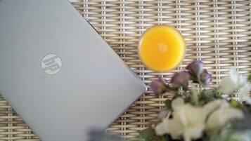 A laptop on a woven surface with a glass of orange juice and a bouquet of flowers.