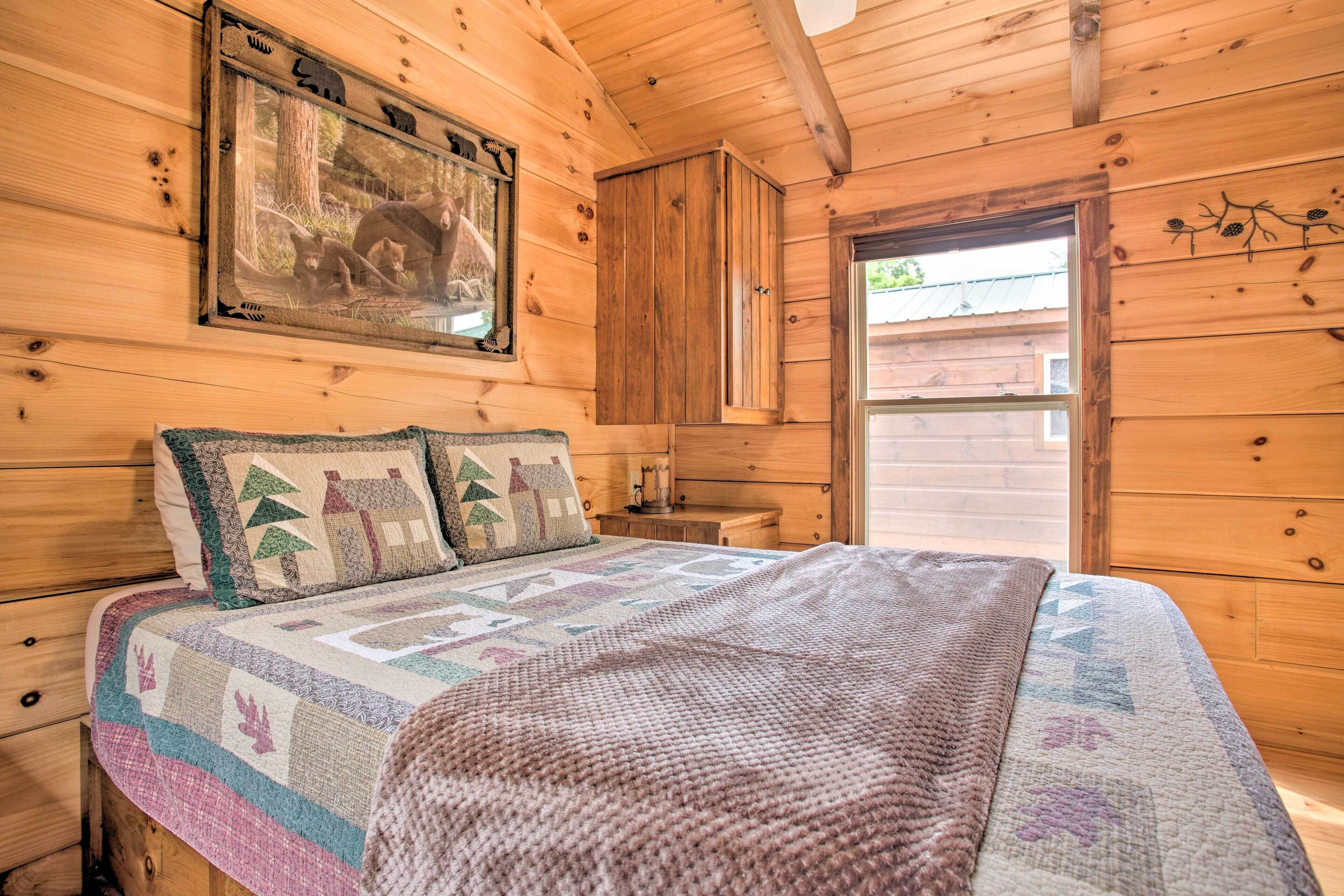A wooden cabin bedroom with a bed, a nightstand, a wooden wardrobe, and a framed picture on the wall.
