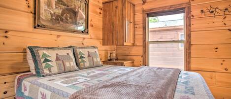 A wooden cabin bedroom with a bed, a nightstand, a wooden wardrobe, and a framed picture on the wall.