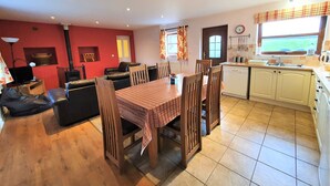 Ein gemütliches Wohnzimmer mit Kamin, eine Essecke mit Tisch und Stühlen, eine Küche mit Fenster und eine rote Wand.