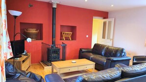Ein Wohnzimmer mit roter Wand, einer schwarzen Ledersofa, einem Holztisch, einer schwarzen TV-Konsole und einem schwarzen Heizgerät.