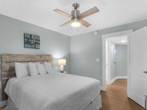 A bedroom with a bed, a ceiling fan, a nightstand with a lamp, and a wall with a motivational quote. - Hidden Dunes Cottages 2-Bedrooms (Miramar Beach)
