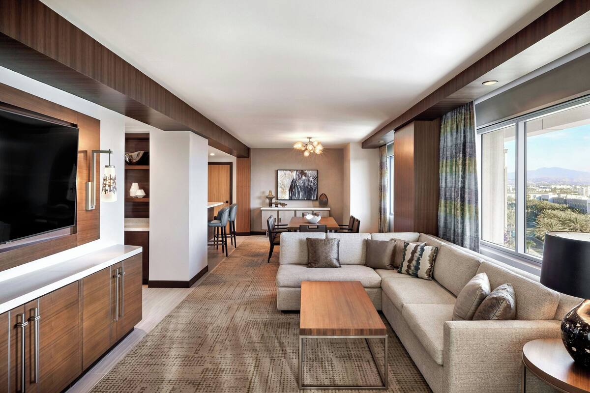 A modern living room with a large flat-screen TV, a sofa, a coffee table, and a dining area with a table and chairs.