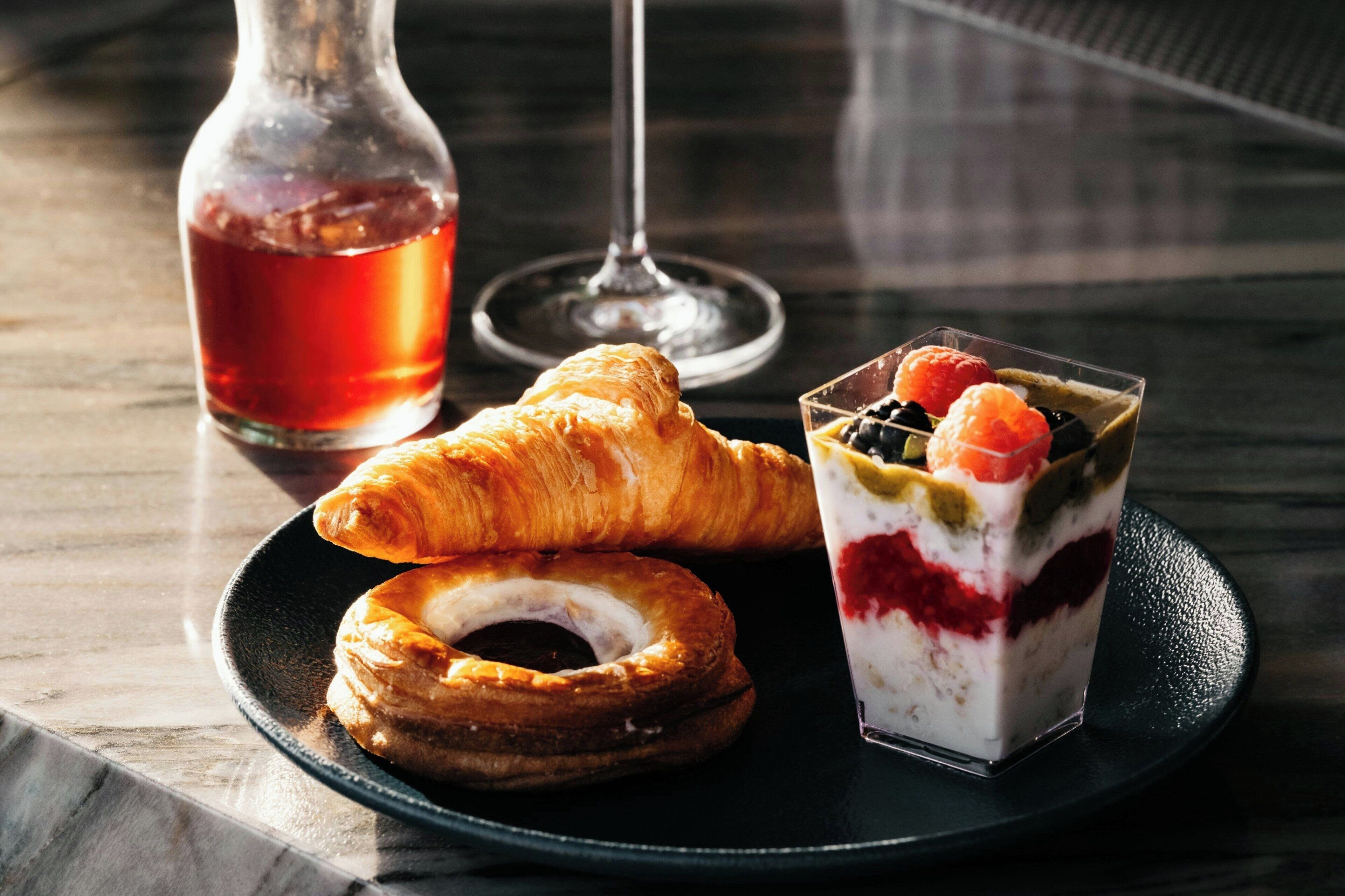 Ein Teller mit einem Croissant, einem Donut und einer gestreiften Dessertkreation mit Beeren und Schokolade.