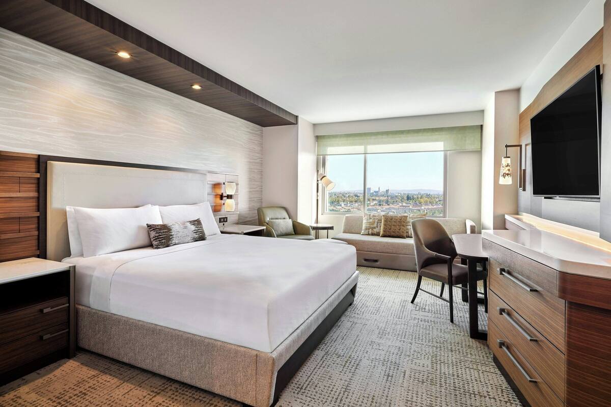 A modern hotel room with a large bed, a desk, a chair, and a TV.