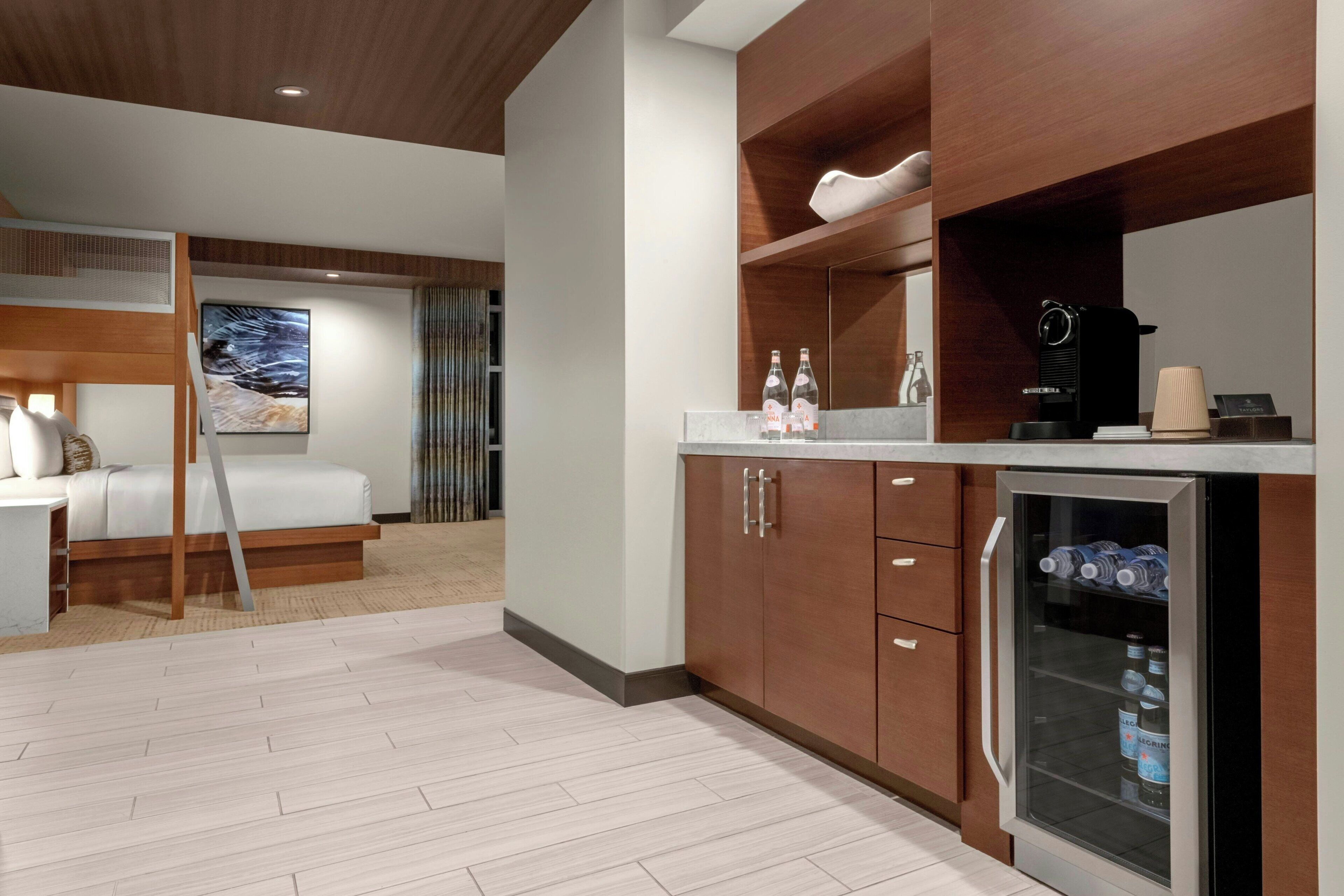 Una habitación de hotel moderna con cama, kitchenette, refrigerador y un amplio ventanal.