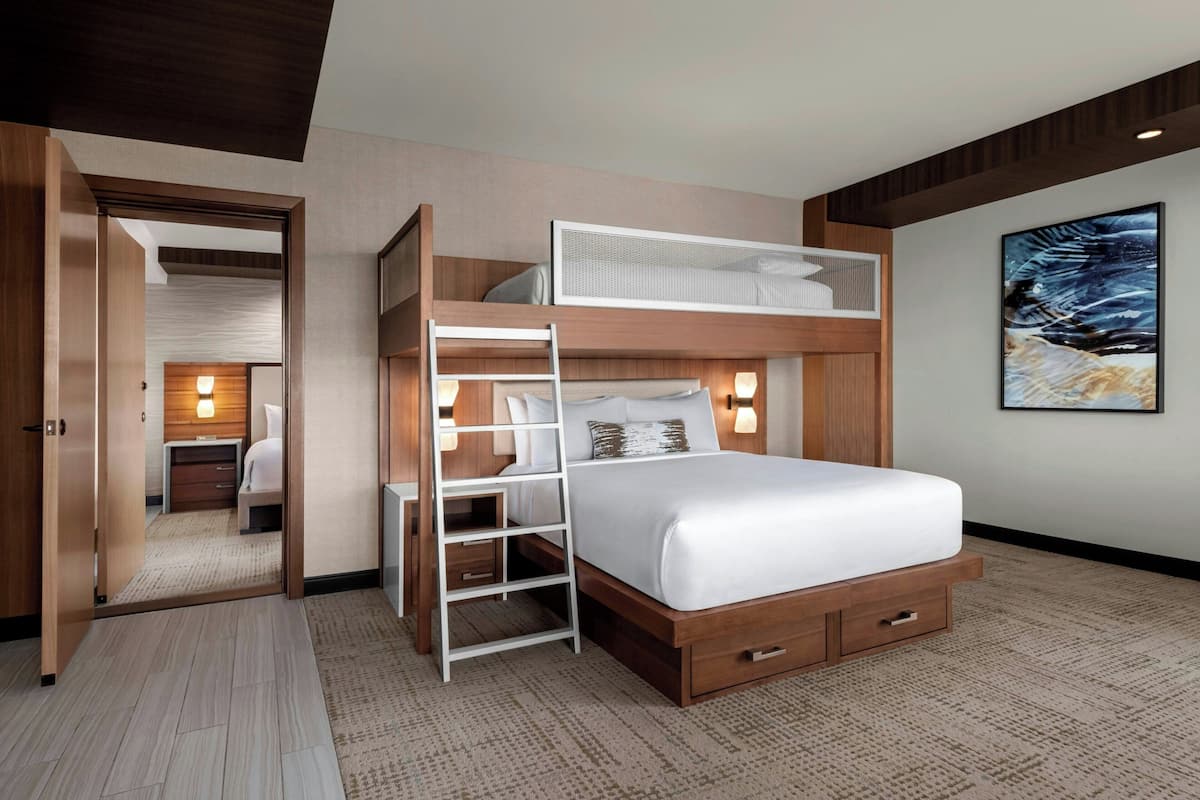 A modern hotel room with a bunk bed, a ladder, a desk, and a nightstand.