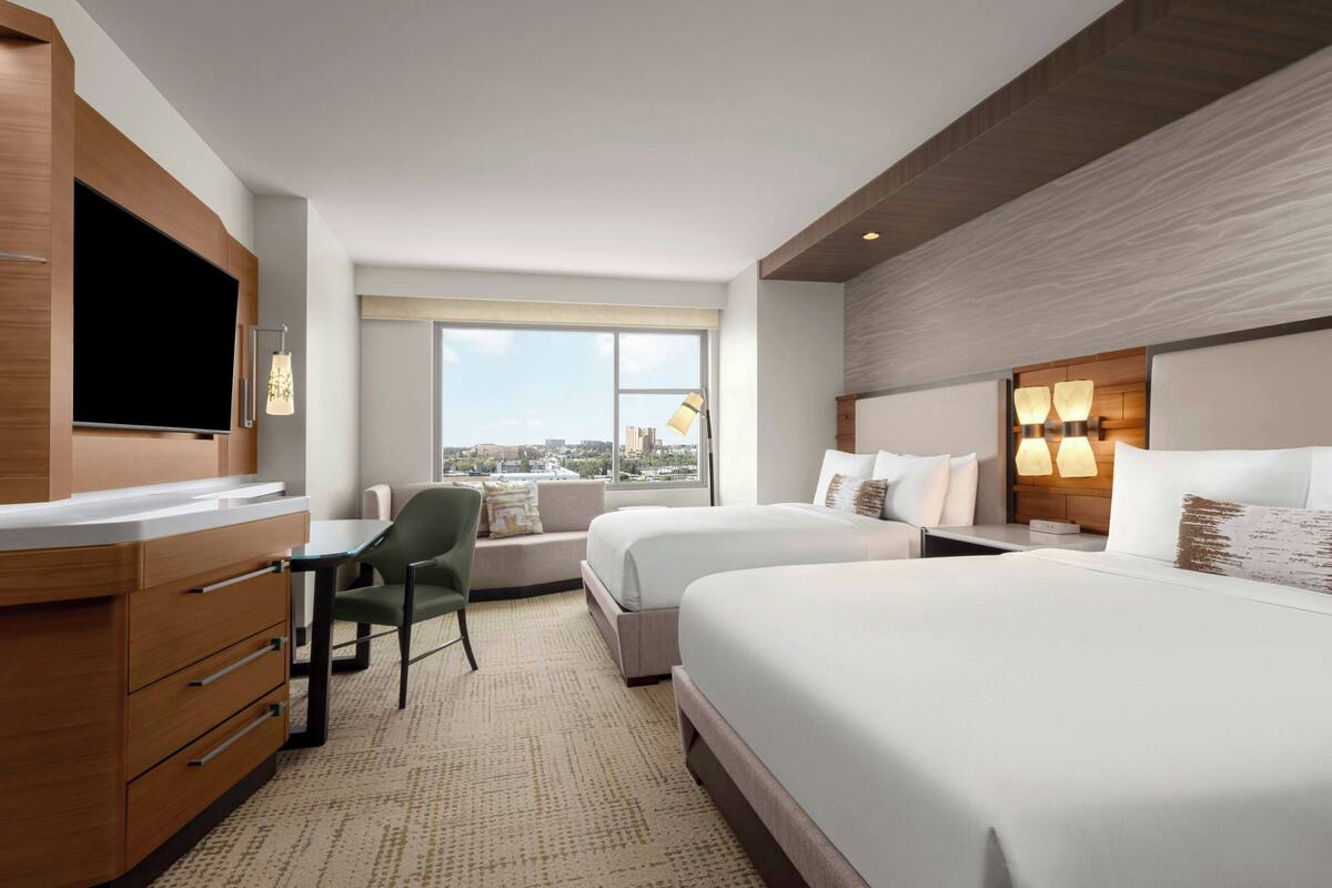 A hotel room with two beds, a desk, a chair, and a TV.