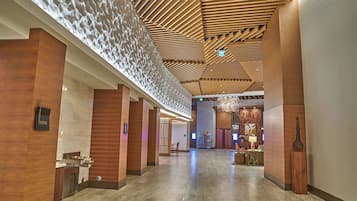 Un amplio vestíbulo de hotel con techo alto, paneles de madera y un mostrador de recepción moderno.