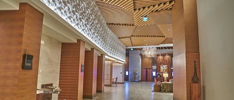 Un amplio vestíbulo de hotel con techo alto, paneles de madera y un mostrador de recepción moderno.