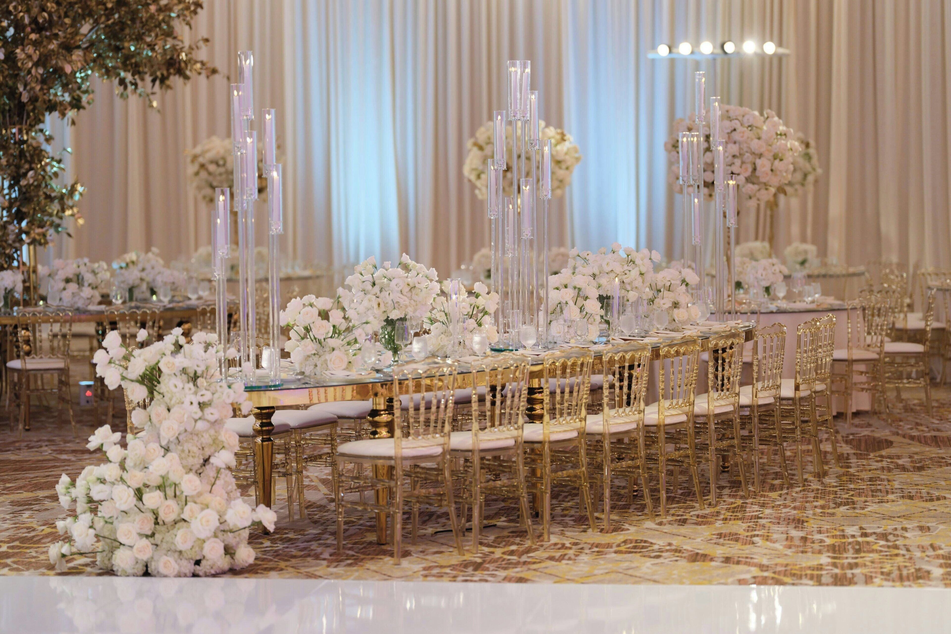 A banquet hall with long tables, gold chairs, and white floral arrangements.
