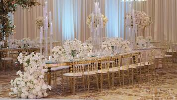 A banquet hall with long tables, gold chairs, and white floral arrangements.