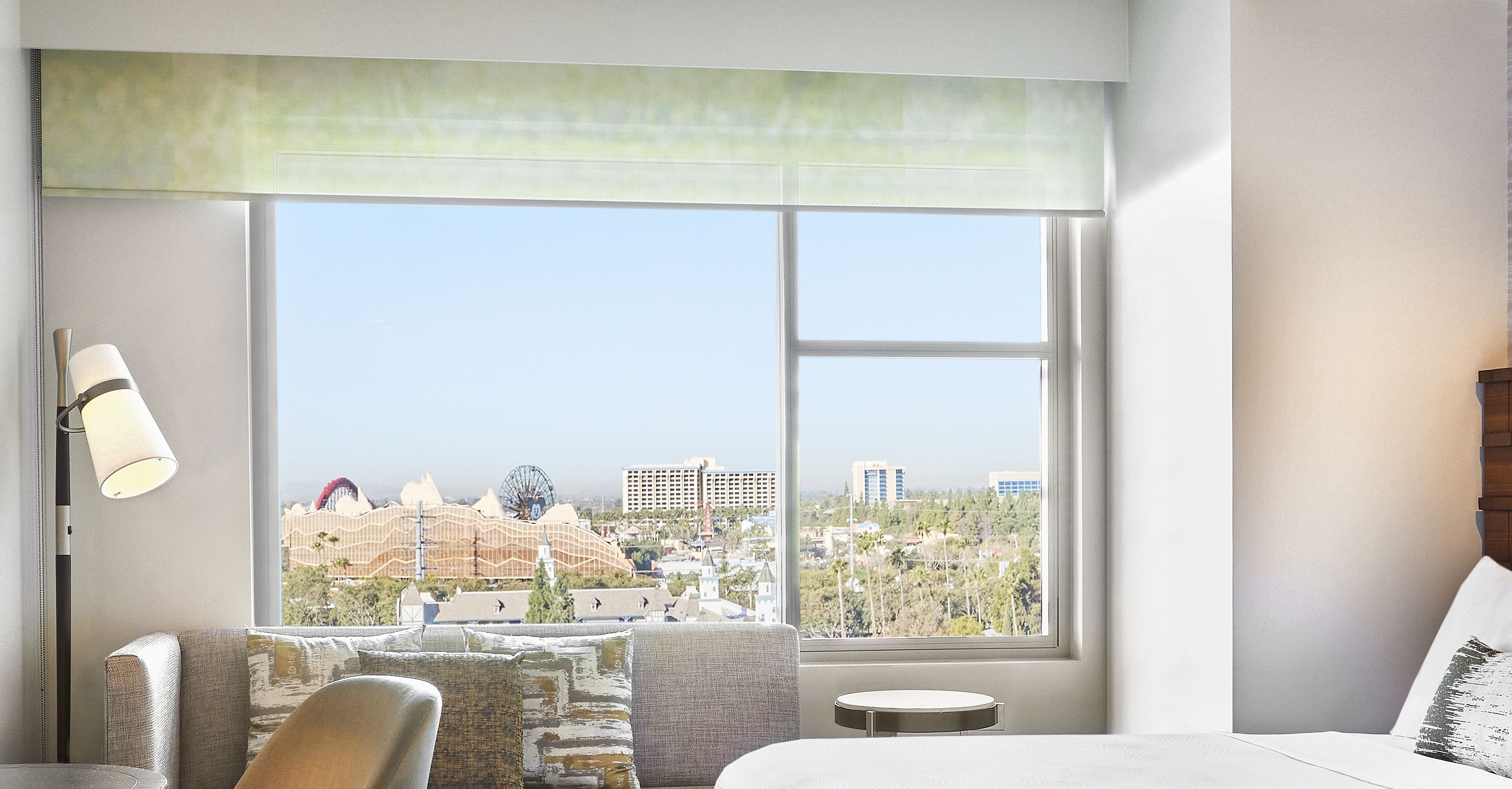 A hotel room with a large window offering a view of a cityscape, including a Ferris wheel and buildings.