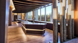 A modern reception area with a central desk, wooden flooring, and large windows offering views of the outdoors. - JW Marriott Anaheim Resort (Anaheim)