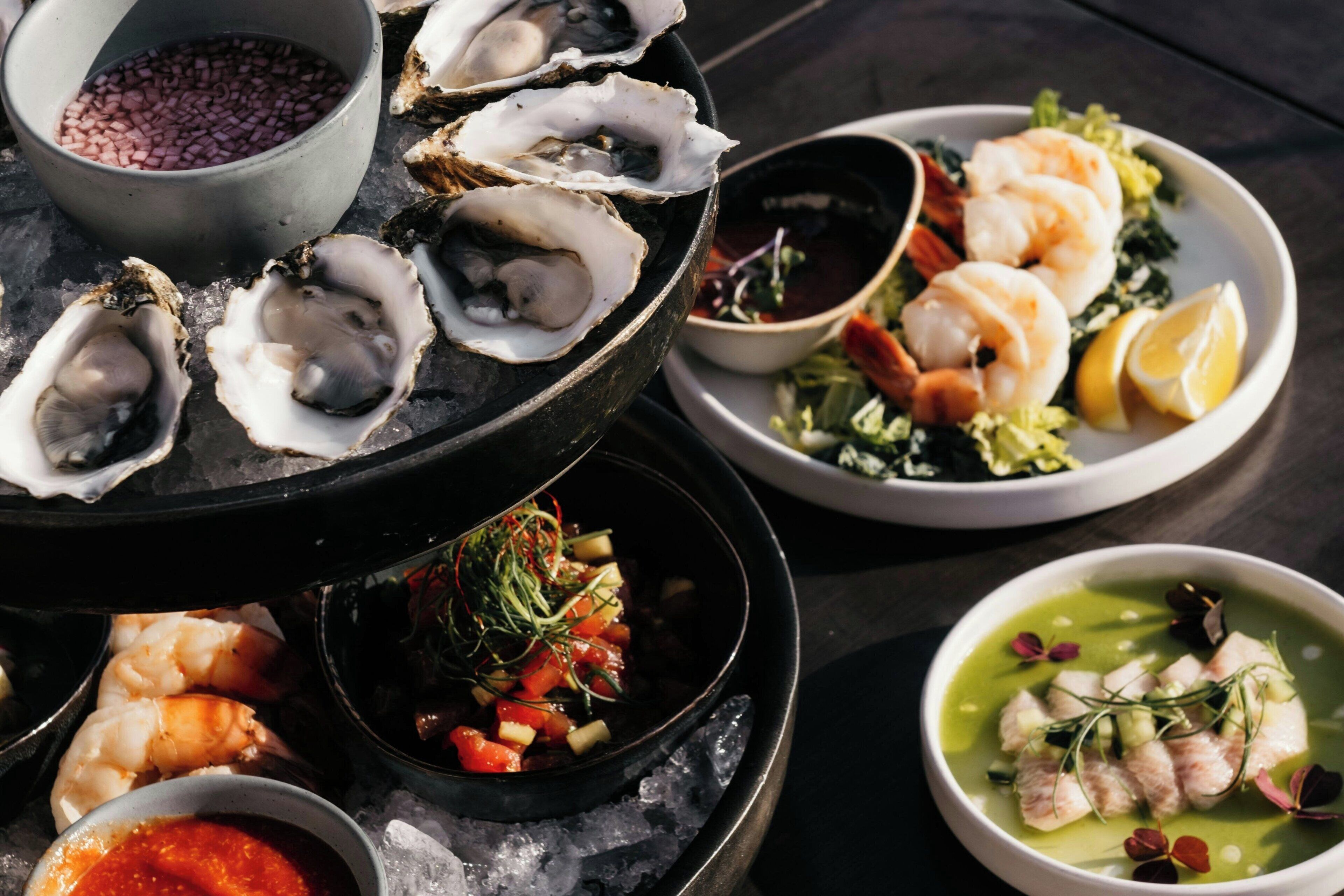 A seafood platter with oysters, shrimp, and a green soup on a table.