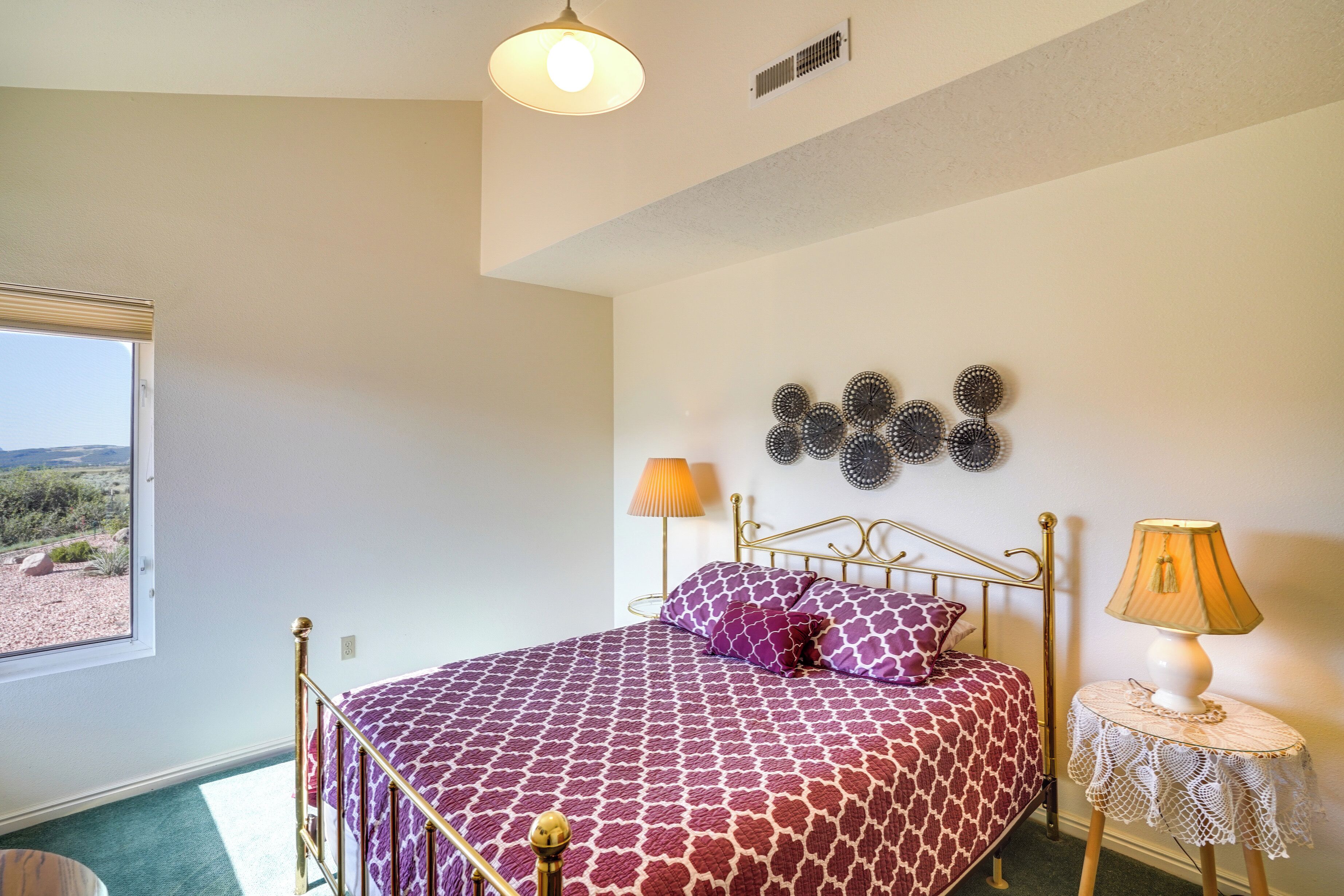 A bedroom with a bed, a window, a wall-mounted lamp, and a small table.