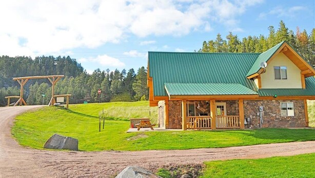 A lodge with a green roof, stone walls, and a wooden porch. - Cottage at Storm Mountain #5 (Hill City)